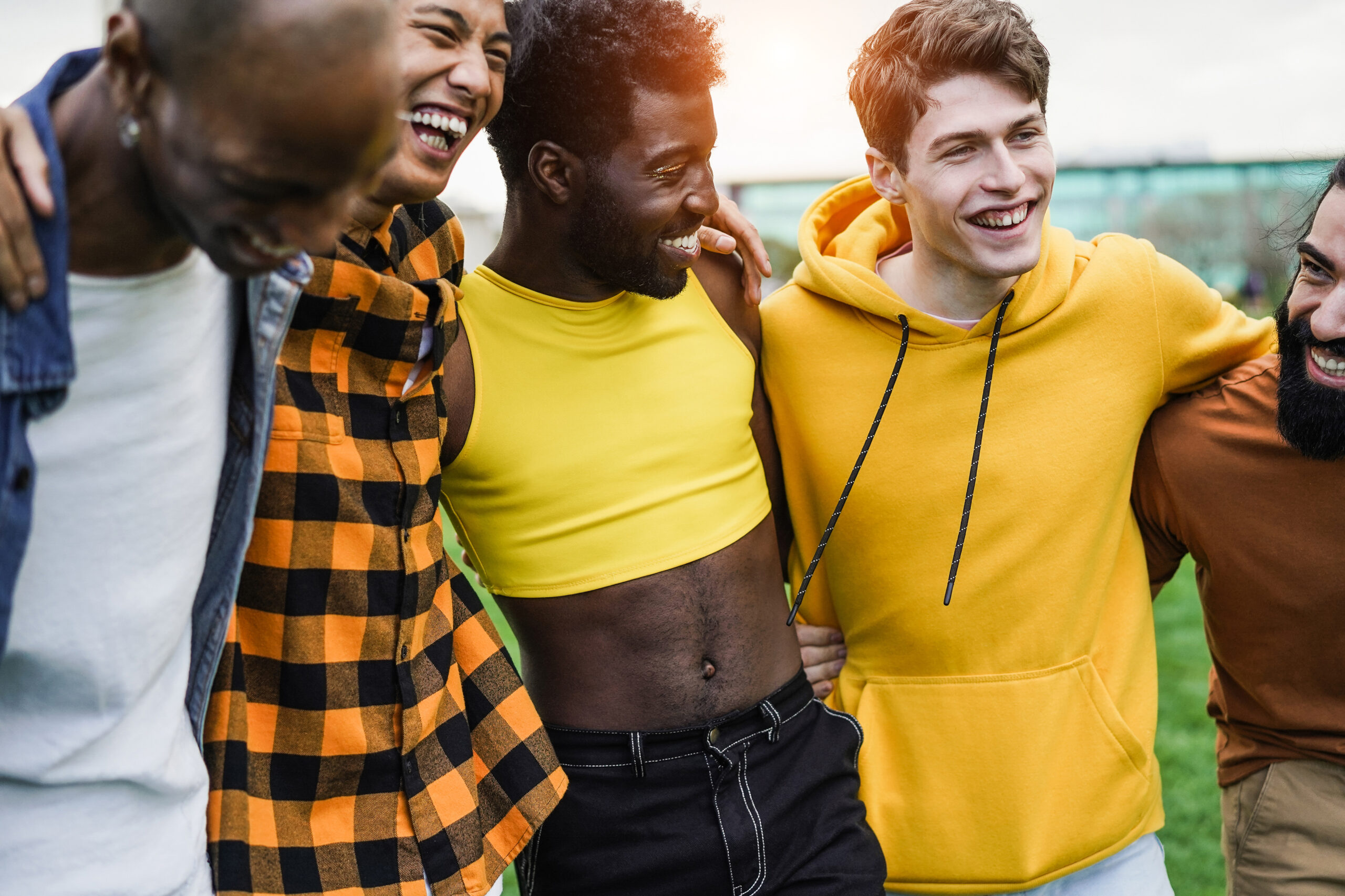 Young diverse men hugging each other at city park - Focus on guy face wearing yellow sweater
